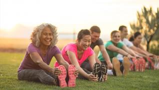 People sitting down on grass, stretching their legs.