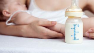 A bottle of breast milk and an adult holding a sleeping child.