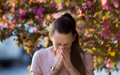 Woman sneezing in front of cherry blossom tree.
