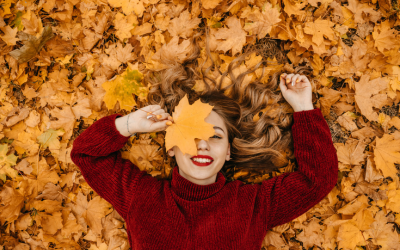 Girl in sweater smiles while laying on fall leaves.