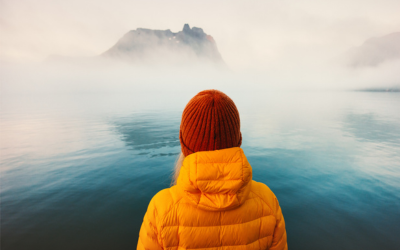Woman in winter coat looks out on foggy waters.