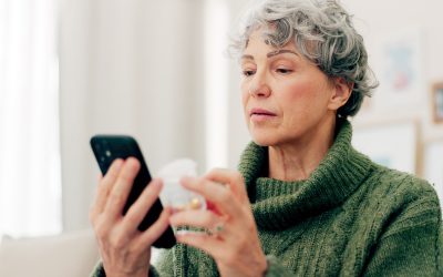 Woman looking at phone while holding supplement bottle.