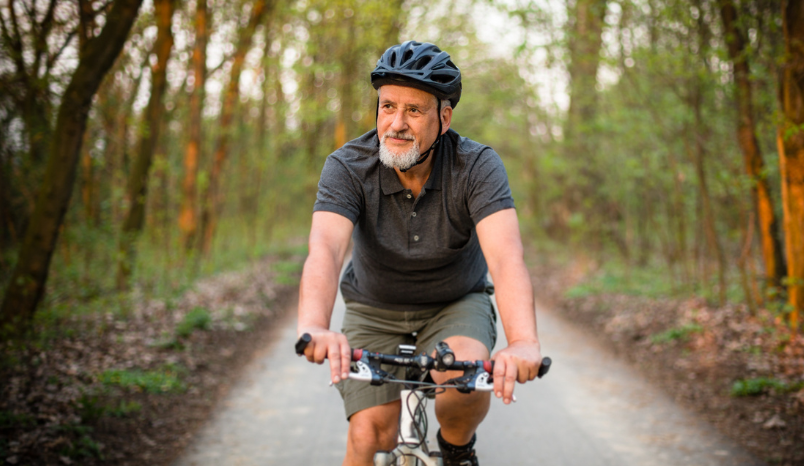 Older man rides mountain bike on forest trail.