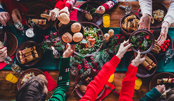 High angle photo of group/family members eating holiday meal, gathered around a table, celebrating winter holiday