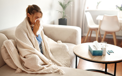 young woman feeling unwell is wrapped snugly in a blanket while sitting on her couch