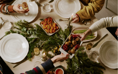 Top down shot of unrecognizable friends at decorated table drinking sparkling wine and eating traditional food for Christmas