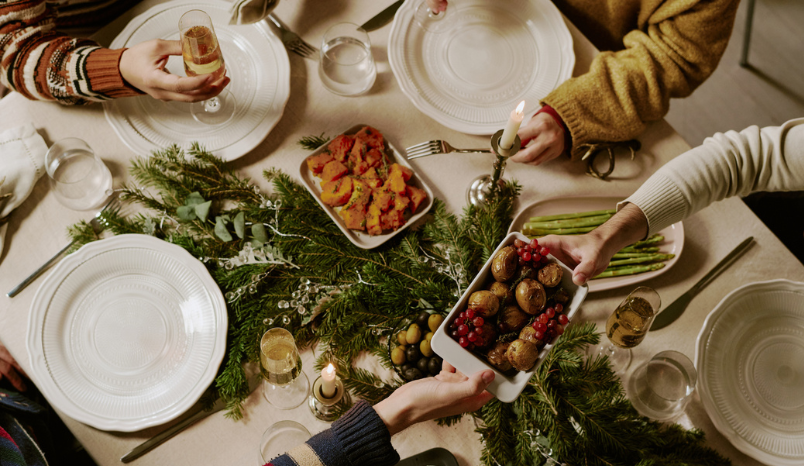 Top down shot of unrecognizable friends at decorated table drinking sparkling wine and eating traditional food for Christmas