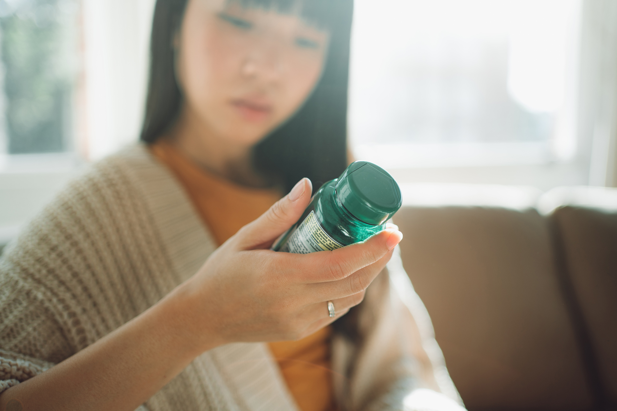 Asian woman looking down at a label on a green pill bottle.