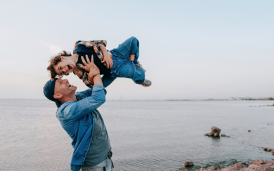 Man on beach lifts young son into the air.