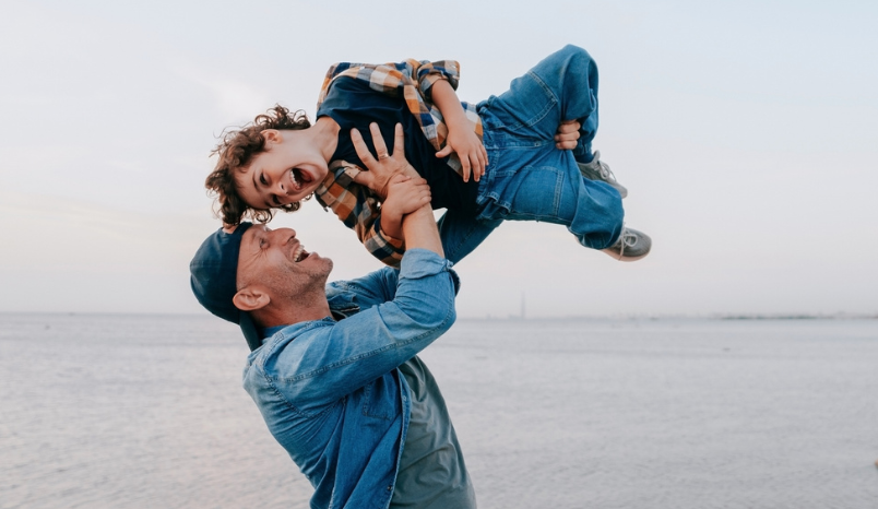 Man on beach lifts young son into the air.