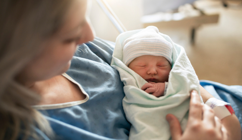 New mom in hospital gown holds newborn.