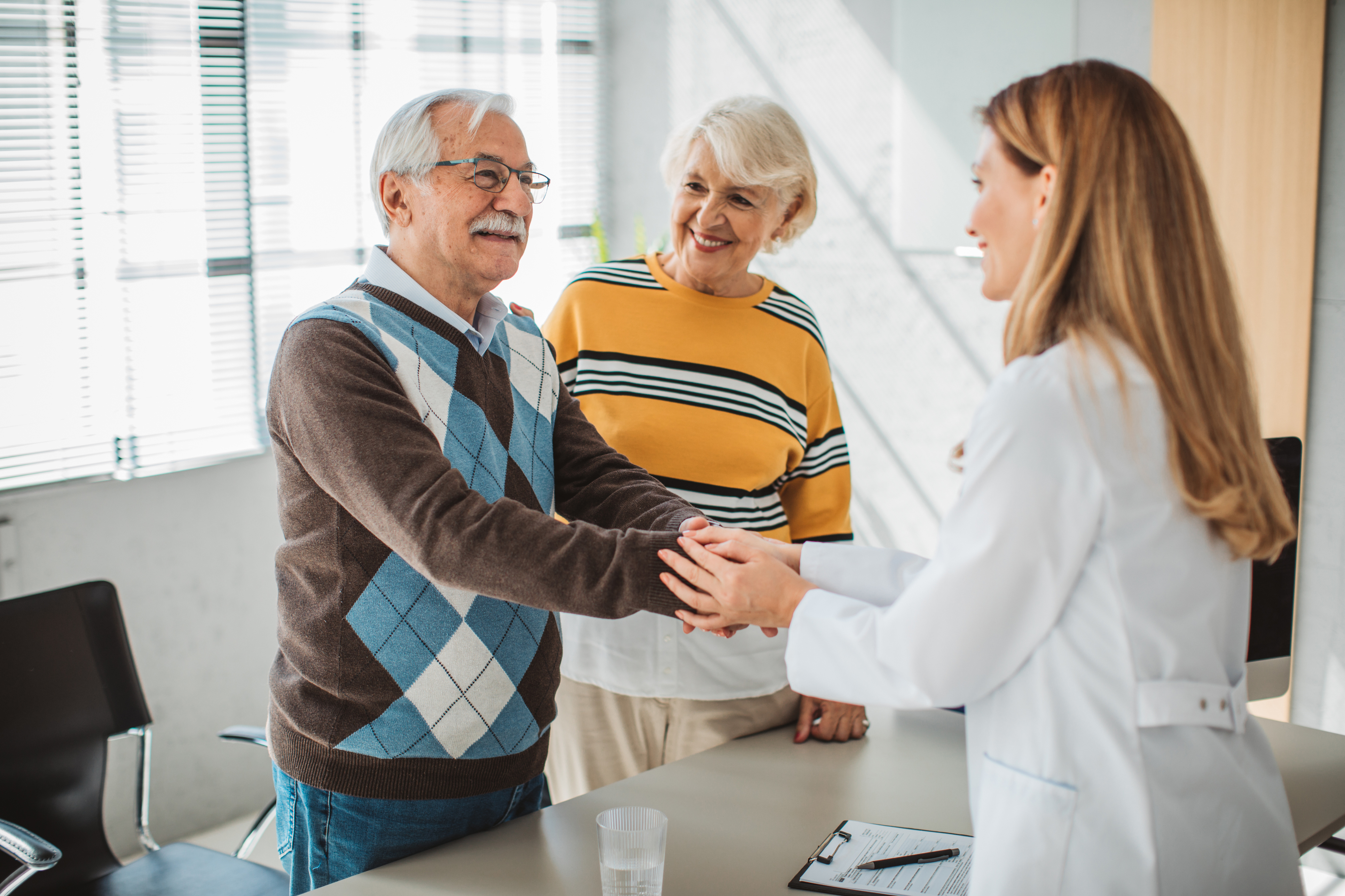 Elder couple, smiling and shaking hands with a healthcare provider.