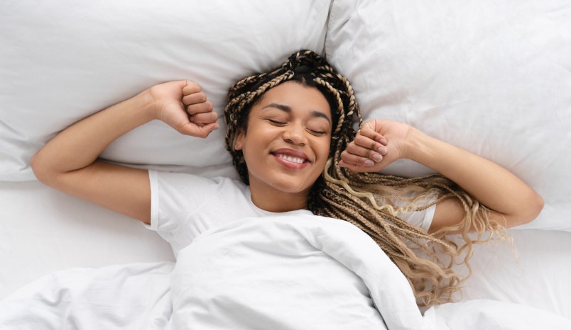 Woman stretches in bed, looking rested.