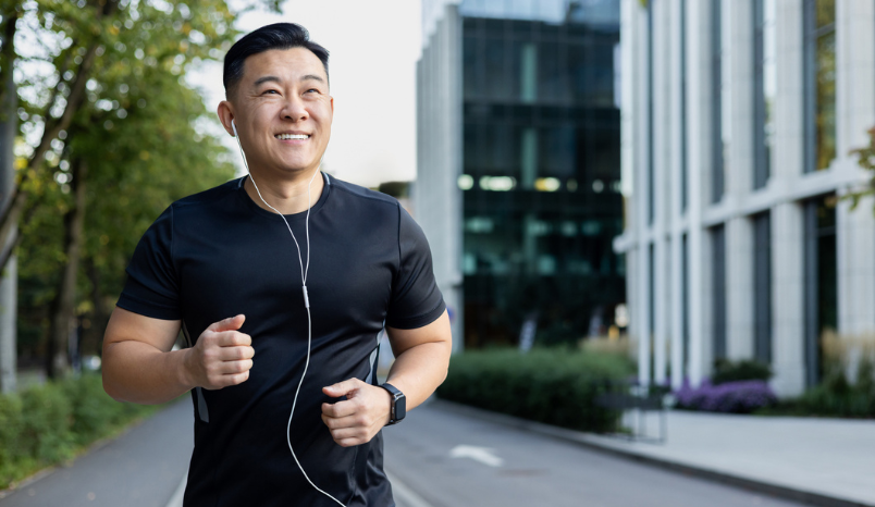 Asian smiling young man doing a morning jog in the city wearing headphones