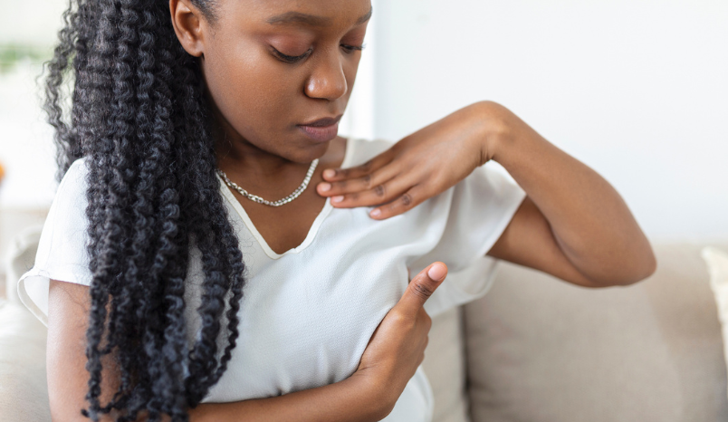 Young African American woman examines breast over shirt.
