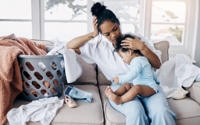 Mom sits on couch with baby next to full laundry bin.