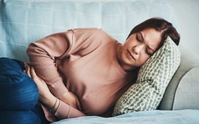 Woman holds stomach in pain and lays on couch.