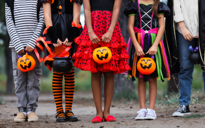 Kids in costume stand outside with trick-or-treat, jack-o-lantern buckets.