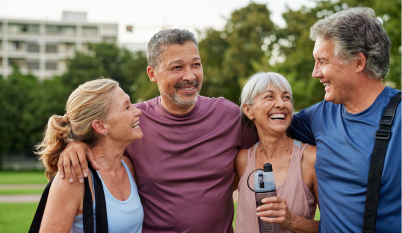 Two mature men and two mature women smiling together outdoors in a park.