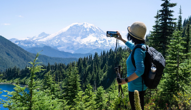  Woman taking photos of snow-capped Mount Rainier using smartphone.