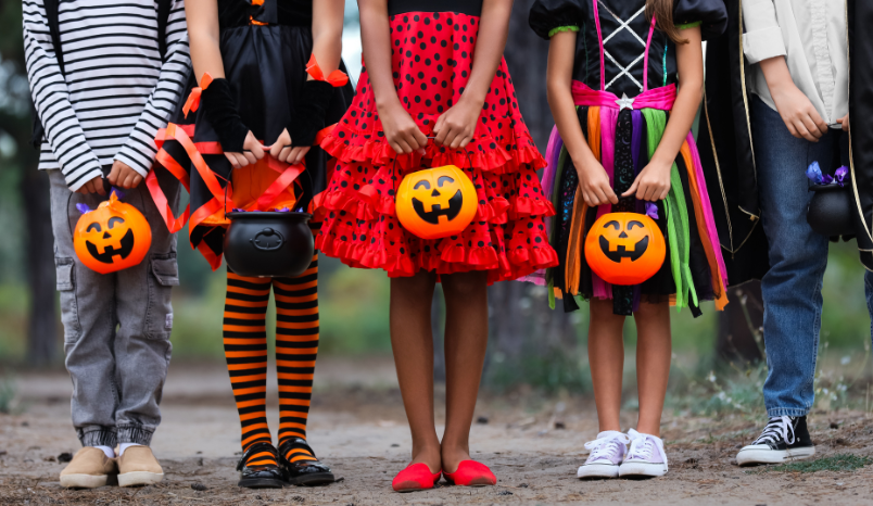 Kids in costume stand outside with trick-or-treat, jack-o-lantern buckets.