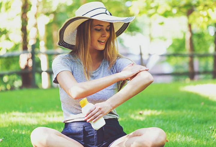 Person applying sunscreen in sun hat