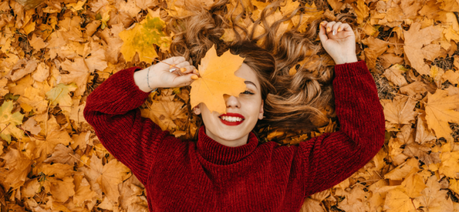 Girl in sweater smiles while laying on fall leaves.