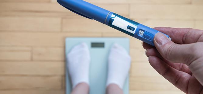 Picture of someone holding weight loss medication standing on a scale