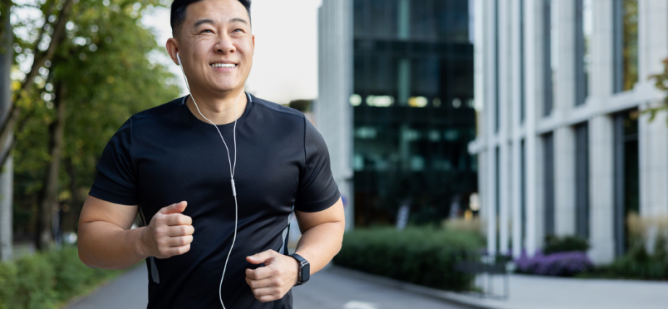 Asian smiling young man doing a morning jog in the city wearing headphones