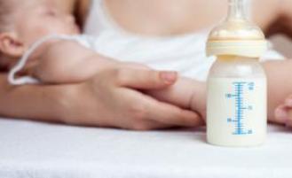 A bottle of breast milk and an adult holding a sleeping child.