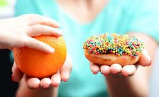 A person holding an orange and a donut in either hand.