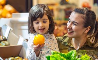 mom-with-young-daughter-in-grocery-store-holding-orange