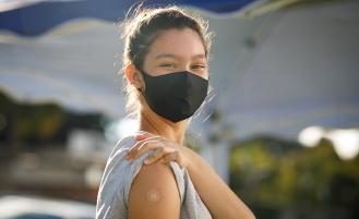 Woman with face mask lifts sleeve to show band-aid.