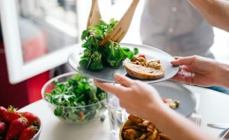 Person places salad on half of a plate using tongs.