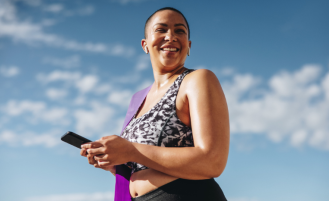 Plus size woman on phone outside with yoga mat.