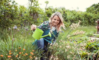Woman waters flowers in garden.