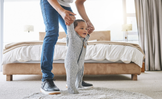 Father holds infant son's hands to walk.