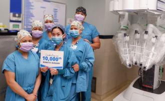 Surgical team stands next to robotic equipment.