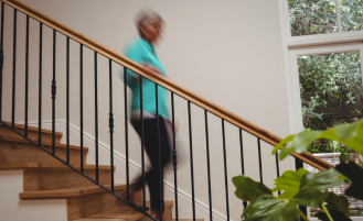 Senior woman walks down stairs in her home.