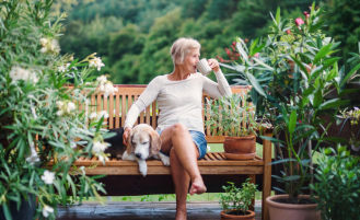 Woman sits on bench with dog while drinking out of a mug.