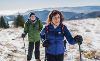 Two older adults snowshoeing on a mountain.