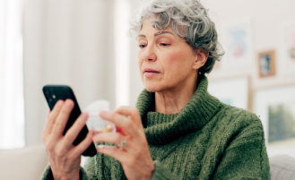 Woman looking at her phone holding supplement bottle.