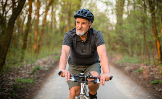Older man rides mountain bike on forest trail.