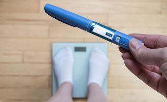 Picture of someone holding weight loss medication standing on a scale