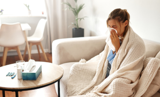 A young woman feeling unwell is wrapped snugly in a blanket while sitting on her couch