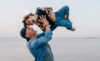 Man on beach lifts young son into the air.