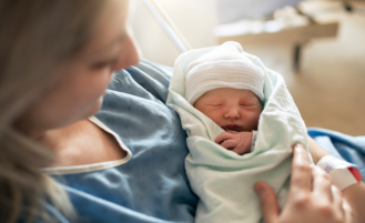 New mom in hospital gown holds newborn.