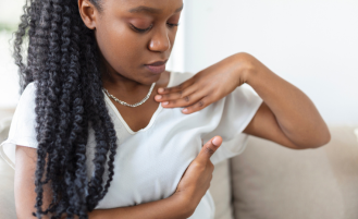 Young African American woman examines breast over shirt.