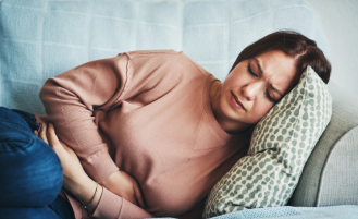 Shot of a young woman experiencing stomach pain while lying on the sofa at home