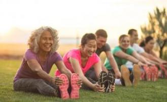 People sitting down on grass, stretching their legs.